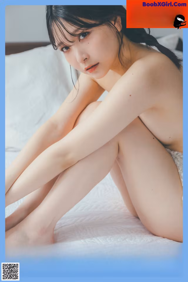 A naked woman sitting on a bed with her legs crossed.