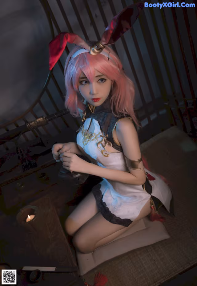 A woman with pink hair sitting on a bed.