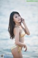 A woman in a gold bikini standing on the beach.