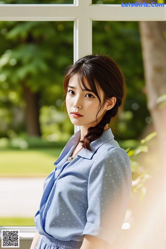 A woman standing in front of a window wearing a blue shirt.