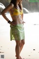 A woman in a yellow bikini standing on a beach.