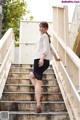 A woman in a white shirt and black skirt standing on some stairs.