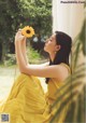 A woman in a yellow dress holding a sunflower.