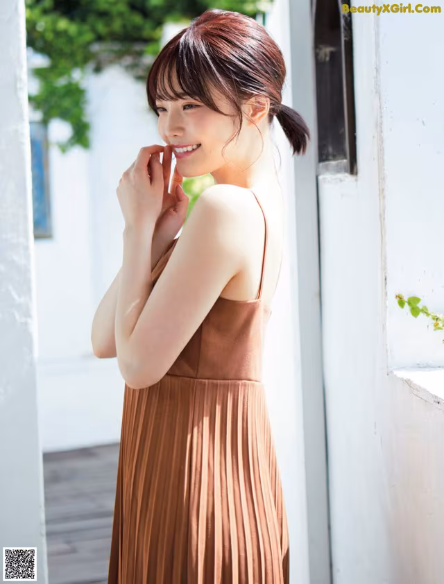 A woman in a brown dress standing by a window.