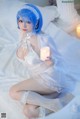 A woman with blue hair sitting on a bed holding a candle.