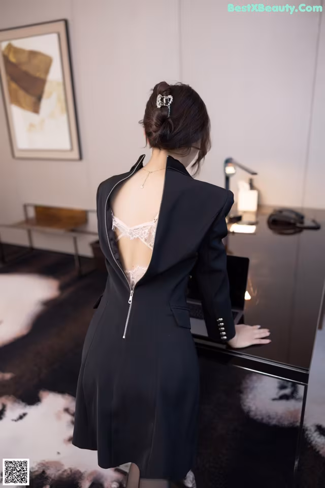 A woman in a black dress standing in front of a desk.