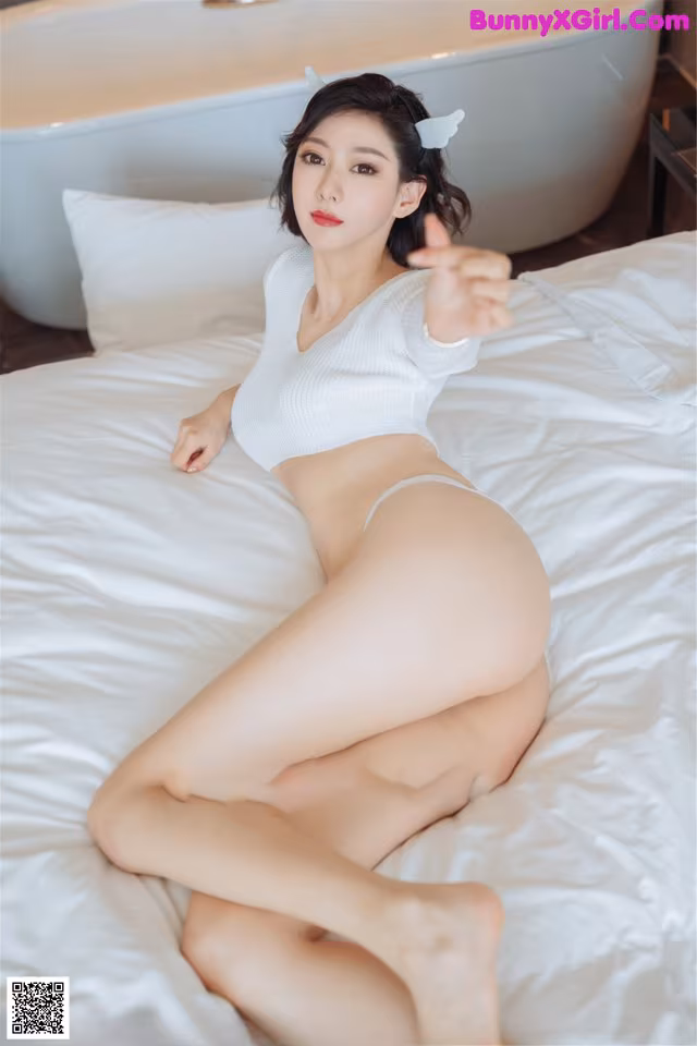 A woman in a white bikini sitting on a bed.