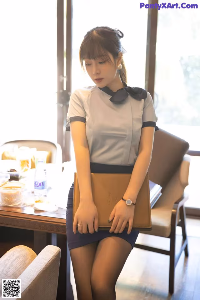 A woman in a gray shirt and black skirt holding a brown purse.