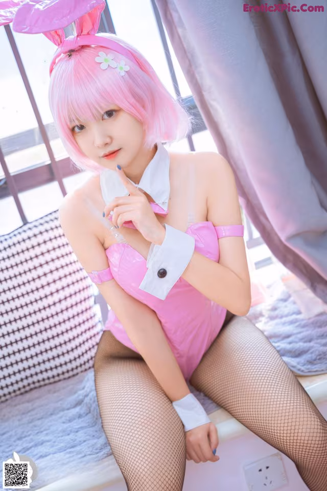 A woman in a pink bunny costume sitting on a bed.