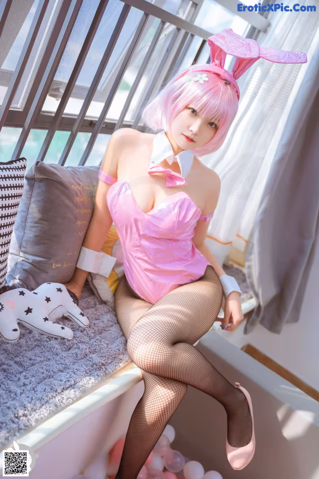 A woman in a pink bunny costume sitting on a bed.
