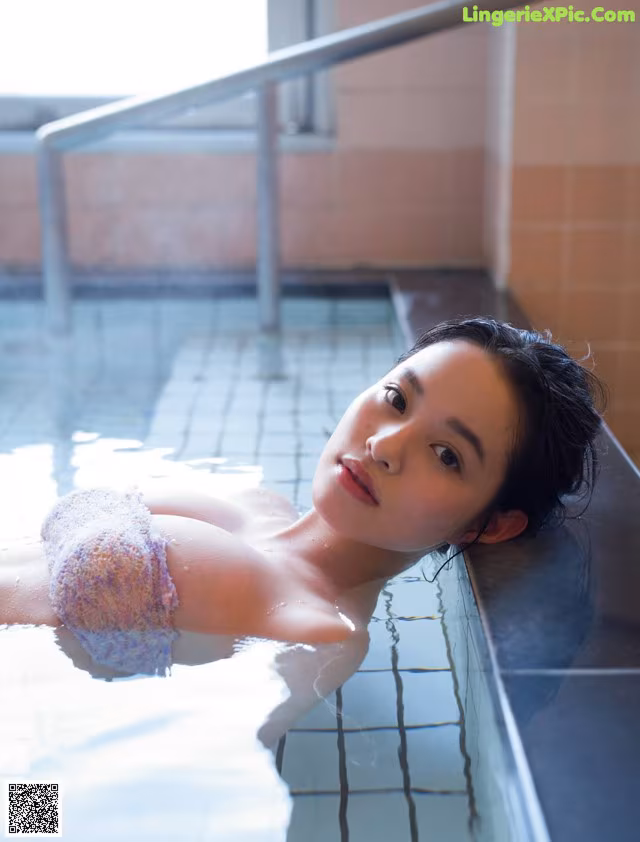 A woman laying in a bathtub with a towel on her head.