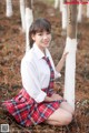 A young woman in a school uniform leaning against a tree.