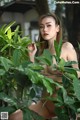 A naked woman sitting in a tree with green leaves.