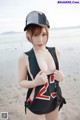 A woman in a black bathing suit and a baseball cap on the beach.