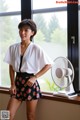 A woman standing in front of a window next to a fan.